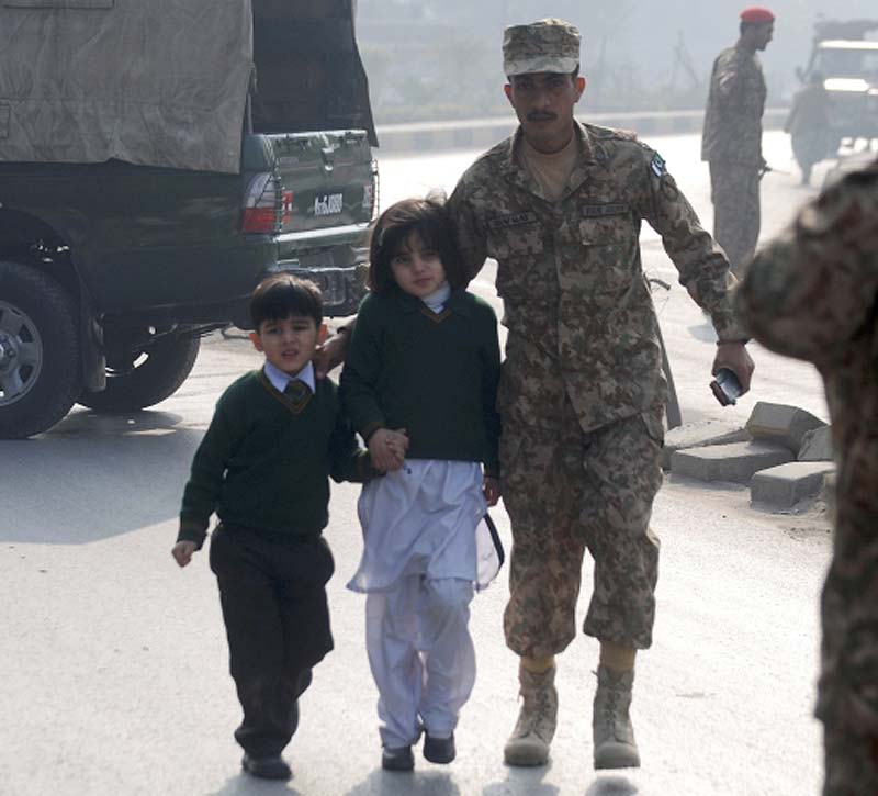 A soldier escorts school students from the Army School that is under attack by Taliban gunmen in Peshawar. Reuters