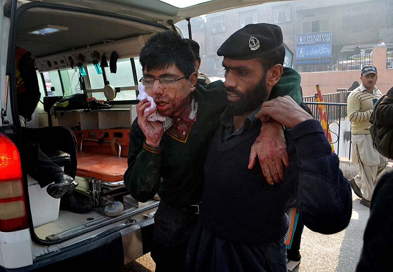 A hospital security guard helps a student injured in the shootout at a school under attack by Taliban gunmen. AP