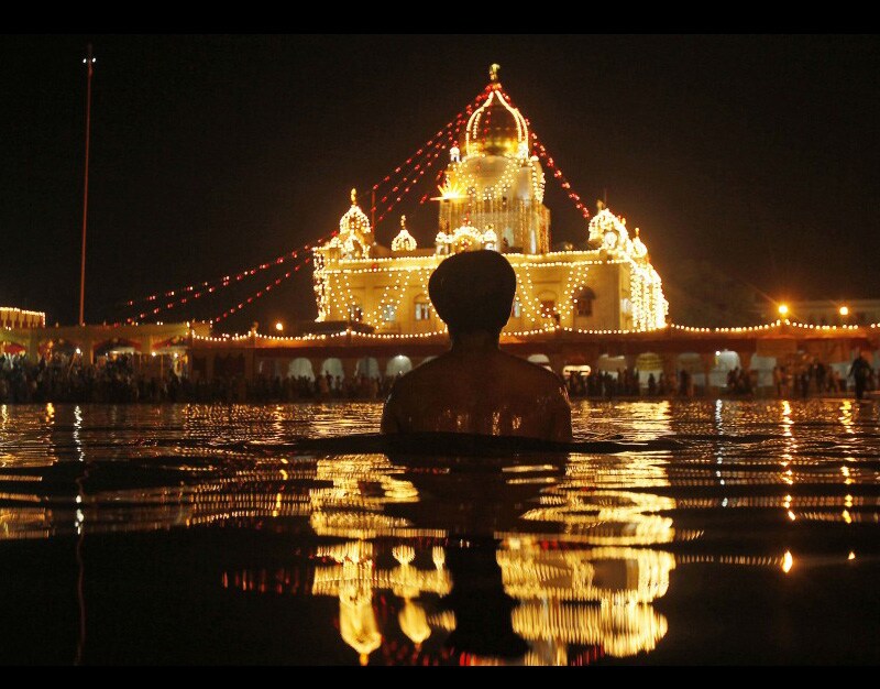 A devotee takes a ritual bath at the water tank of the illuminated Bangla Sahib Sikh temple on the birth anniversary of Guru Nanak in New Delhi, India. (AP)