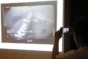 A journalist takes a photograph of an image believed to be of the fuselage of AirAsia Flight QZ8501 taken by an underwater ROV provided by the Singapore Navy, during a news conference at the Indonesian National Search and Rescue Agency in Jakarta January 14, 2015. (Reuters)
