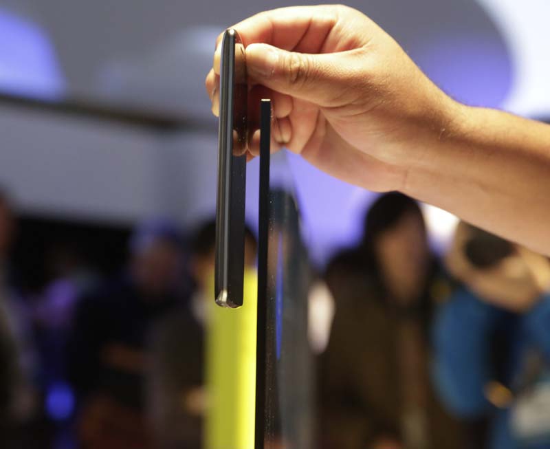 An attendee places his smartphone next to Sony's 65-inch X900 C series 4K Ultra HD TV to compare the thickness at the Sony booth at the International CES Monday, Jan. 5, 2015, in Las Vegas. The display is less than 0.2 inches thick at its slimmest point. (AP)