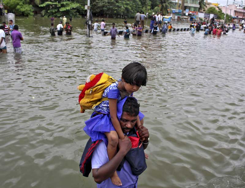 Chennai Floods: Heavy rains continued to lash coastal Cuddalore district, one of the worst affected areas ever since North-East monsoon fury started early last month, and Villupuram and Kanyakumari districts and Puducherry as the death toll in the state mounted to 269. <br>Image Caption: A man carries a girl through a flooded road in Chennai. (Reuters)</br>