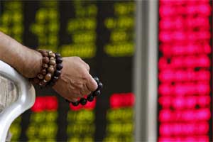 An investor holds onto prayer beads as he watches a board showing stock prices at a brokerage office in Beijing. (Photo: Reuters)