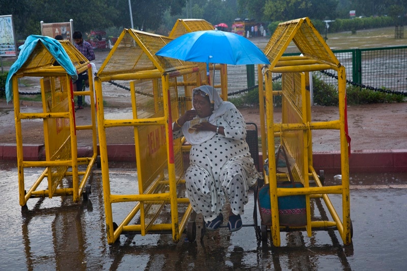 An Indian woman eats a snack sitting in between police barricades during monsoon rains on Tuesday. The monsoon arrived in India on June 8 and is likely to deliver 106 percent rainfall of a long-term average this year. (AP)