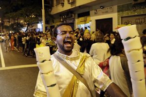 Cyrus Oliveira yells as he runs with torches for sale while others wait to see the Olympic torch in the streets of Copacabana on its journey to the opening ceremony of the 2016 Summer Olympics in Rio de Janeiro, Brazil, early Friday, Aug. 5, 2016. (AP Photo/Gregory Bull)