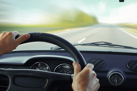 Driver in car holding steering wheel. Blurred road and sky