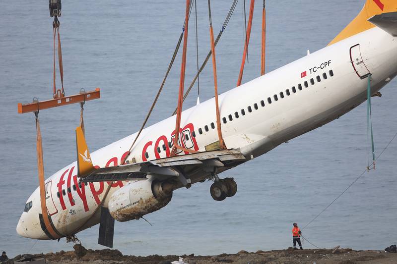 A worker guides a crane lifting a Boeing 737-800 of Turkey's Pegasus Airlines from a slope in Trabzon, Turkey, Thursday, Jan. 18, 2018. Turkish authorities lifted the passenger plane that skidded off a runway in northern Turkey and stopped on the side of a slope meters away from the Black Sea late Saturday. All passengers and crew were evacuated and no one was injured.(AP Photo/Lefteris Pitarakis)