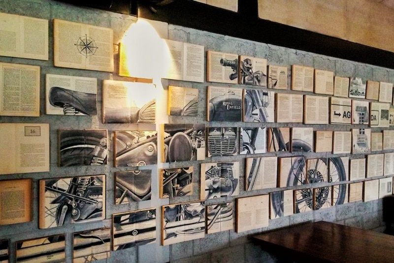 The reading room of the Royal Enfield Garage Cafe has this uniquely designed wall that has been done by a street artist from Mumbai. The place is designed on the theme of a reader's room and you will find multiple books glued on the wall. What's more interesting is the presentation of a Royal Enfield motorcycle through these open books.