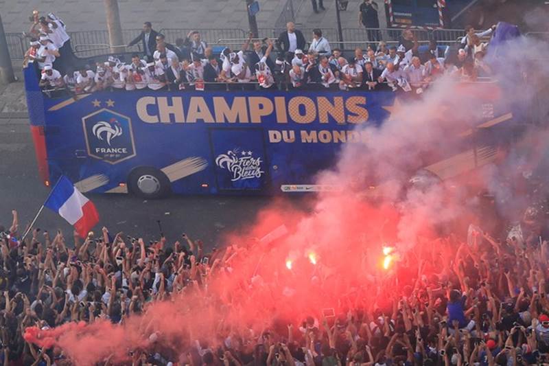 French soccer players waves from a bus in a cloud of smoke during a parade on the famed Champs Elysees avenue in Paris. Crowds began converging early Monday on the Champs Elysees, the gathering point for all national celebrations, for a parade by the team atop an electric bus.