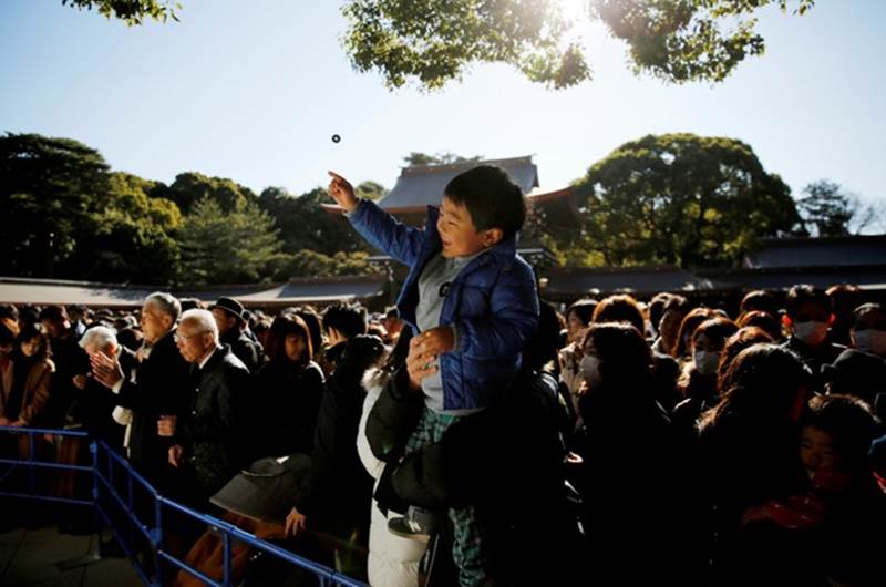 A boy throws a coin as he offers prayers on on January 1, 2019 at Meiji Shrine in Tokyo, Japan (Reuters)