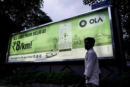 A pedestrian walks past an advertisement for the Ola ride-hailing service and application, owned by ANI Technologies Pvt., in New Delhi, India, on Saturday, Sept. 19, 2015. Ola, the operator of an Indian taxi-hailing app, will lease cars to boost the number of vehicles in its network to stave off competition from Uber Technologies Inc. Photographer: Dhiraj Singh/Bloomberg