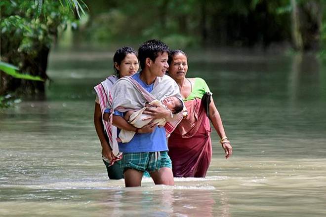 A man carries his new born baby as he and his family members wade through a flooded area to reach a relief camp at a village in Assam's Barpeta district of Assam (Reuters photo)