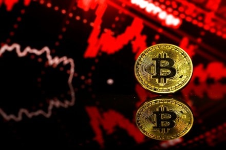 FILE: A coin representing Bitcoin cryptocurrency sits reflected on a polished surface and photographed against a photo illustration of electronic data indicating stocks falling in this arranged photograph in London, U.K., on Thursday, Feb. 8, 2018. The great cryptocurrency crash of 2018 is heading for its worst week yet. Bitcoin sank toward $4,000 and most of its peers tumbled on Friday, extending the Bloomberg Galaxy Crypto Indexs weekly decline to 25 percent. Thats the worst five-day stretch since crypto-mania peaked in early January. Photographer: Luke MacGregor/Bloomberg