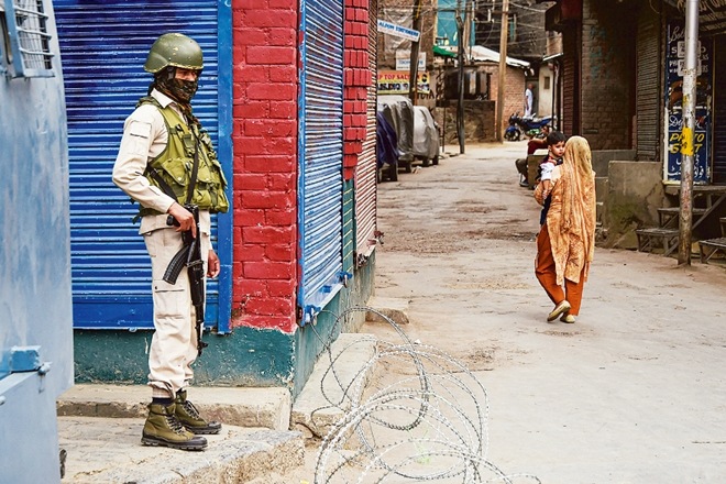 A security official stands guard near a temporary barricade in Srinagar as a woman passes by (PTI Image) A security official stands guard near a temporary barricade in Srinagar as a woman passes by (PTI Image)