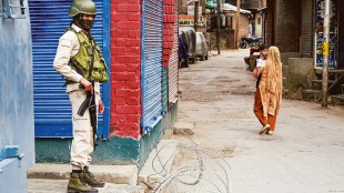 A security official stands guard near a temporary barricade in Srinagar as a woman passes by (PTI Image)
