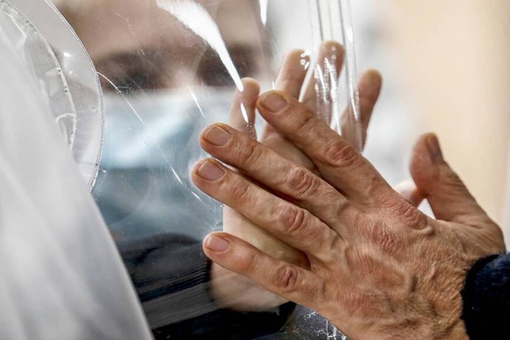 Relatives touch each other's hands through a plastic film screen and a glass to avoid contracting Covid-19 in Rome. (Cecilia Fabiano/LaPresse via AP, File)