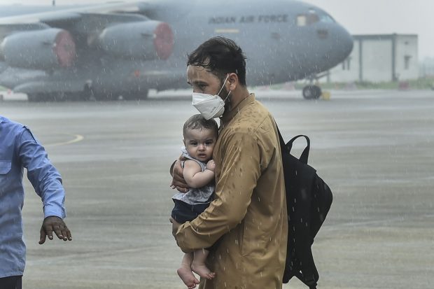 A man carries a child as people who were stranded in crisis-hit Afghanistan arrive by a special repatriation flight of IAF at the Hindan Air Force Station, in Ghaziabad on August 22, 2021. (PTI Photo)