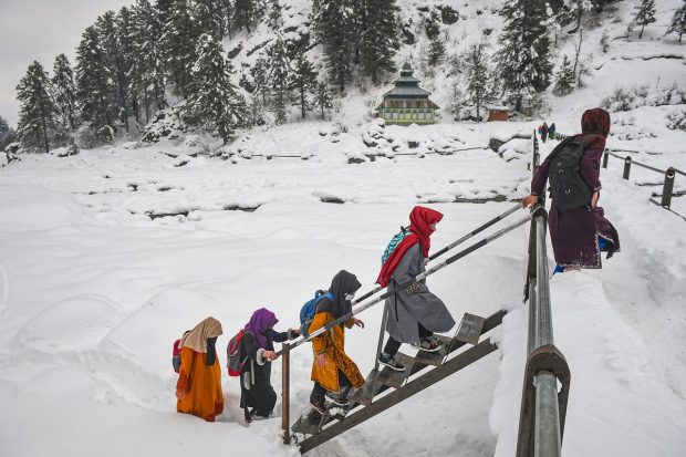 Students walk through snow as they return from a government tuition centre, after recent snowfall at a village at Tangmarg in Baramulla district. (PTI Photo)
