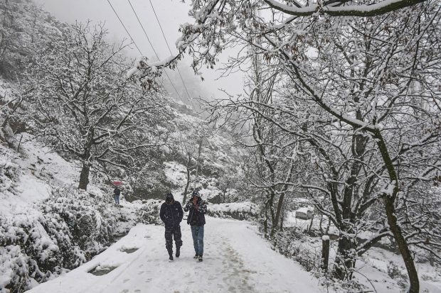 Men walk on a road during season's first snowfall, on the outskirts of Srinagar. (PTI Photo)