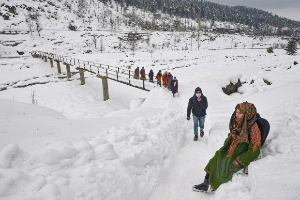 A student sits down to rest as others walk through snow while returning from a government tuition centre, after recent snowfall at a village at Tangmarg, in Baramulla district. (PTI Photo)