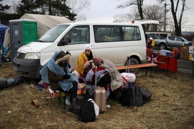 Women sit next to their luggage after fleeing from Russia's invasion of Ukraine, at the border crossing in Siret, Romania. (Reuters Photo)