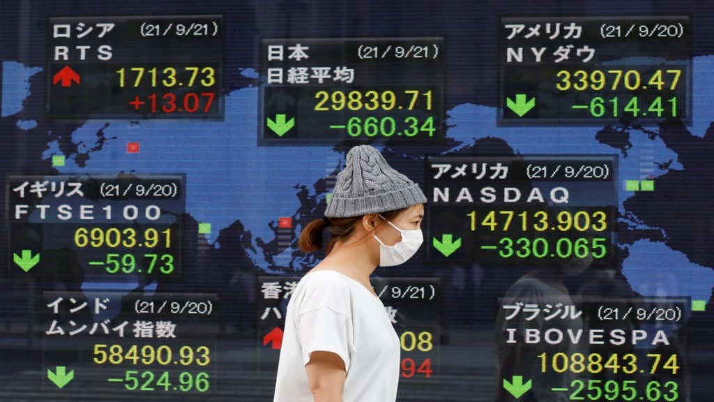 A woman wearing a protective mask, amid the COVID-19 outbreak, walks past an electronic board displaying Japan and other countries' stock indexes outside a brokerage in Tokyo, Japan. (File Photo: Reuters)