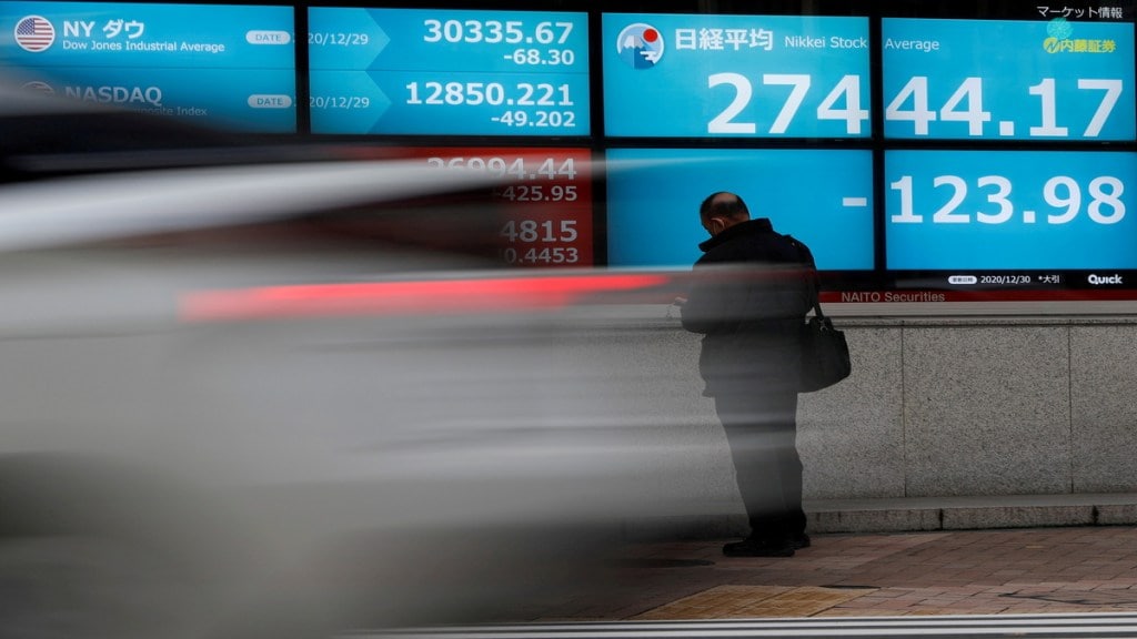 FILE PHOTO: A man stands in front of a screen displaying Nikkei share average and the world's stock indexes outside a brokerage, amid the coronavirus disease (COVID-19) outbreak, in Tokyo, Japan December 30, 2020. REUTERS/Issei Kato//File Photo