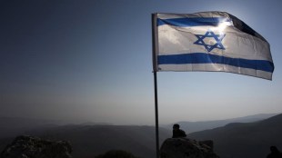 Israeli soldier stands guard under an Israeli national flag during a tour made by Israeli parliament members in the Jordan Valley near the Jewish settlement of Maale Efrayim