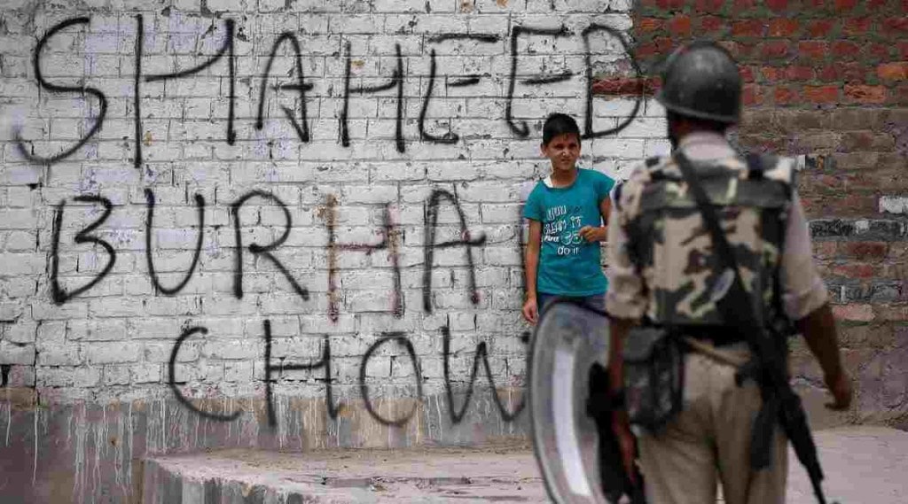 A boy stands next to a wall painted with graffiti as an Indian policeman stands guard during a protest in Srinagar against the recent killings in Kashmir, July 22, 2016. | Danish Ismail/Reuters