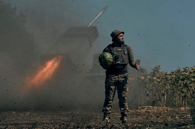 A Ukrainian soldier holds a watermelon and thumbs up as a rocket launch system fires in the font line in Donetsk region, eastern Ukraine, Saturday, Aug. 3, 2022. (AP Photo)