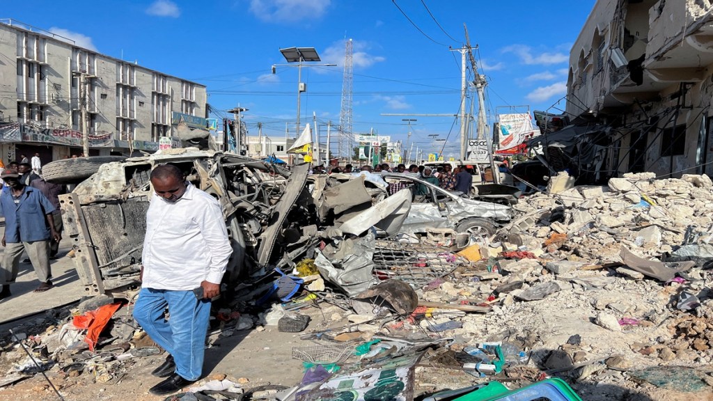 A man walks past wreckages of destroyed vehicles near the ruins of a building at the scene of an explosion along K5 street in Mogadishu, Somalia (Reuters image)