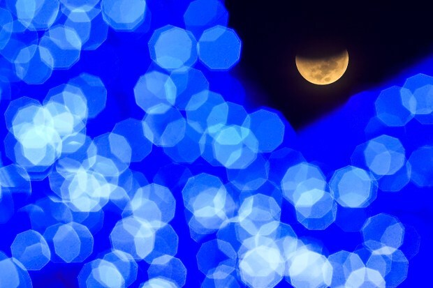 Seen past Christmas lights, the Earth's shadow starts to cover the moon during a lunar eclipse, at a public square in Caracas, Venezuela, early Tuesday, Nov 8, 2022. (Photo source: AP)