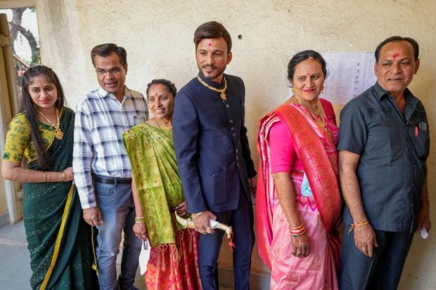 Indian groom Kavit Patel, third right, along with his family stands in queue to cast his vote during the first phase of Gujarat state legislature elections in Limbdi. (Image/PTI)