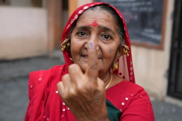 A woman shows her inked finger after casting her vote during the first phase of Gujarat state legislature elections. (Image/PTI)