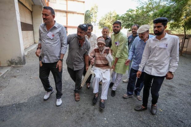 An elderly man is carried by others as he arrives to cast his votes during the first phase of Gujarat state legislature elections in Limbdi. (Image/PTI)