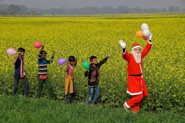 A man dressed as Santa Claus takes a walk with children through a farm field, in Nadia, India on Saturday. (Image: PTI)