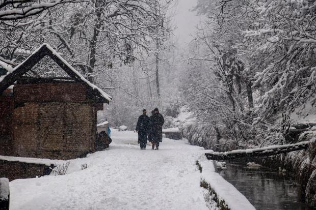  People walk on a snow-covered road during fresh snowfall in Tangmarg area of North Kashmir (PTI Photo) 