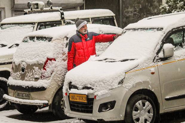 Joshimath: A man clears snow from a car after heavy snowfall in Joshimath. (PTI Photo)