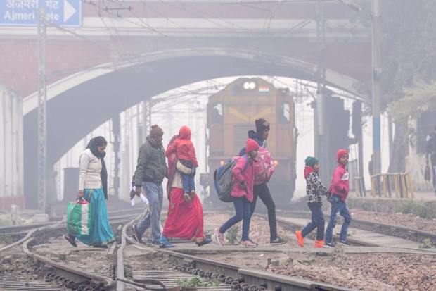 Passengers cross railway tracks at New Delhi railway station amid low visibility due to a thick layer of fog on a cold winter morning, in New Delhi (PTI Photo)