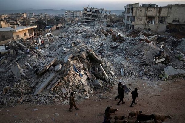 People walk past collapsed buildings following a devastating earthquake in the town of Jinderis, Aleppo province, Syria, Thursday, Feb. 9, 2023. (Image: AP Photo/Ghaith Alsayed)