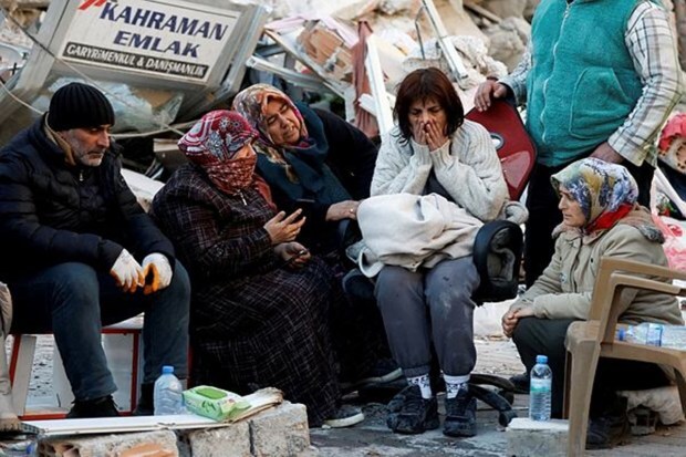 People sit next to rubble at the site of a collapsed building in the aftermath of a deadly earthquake, in Kirikhan, Turkey on Feb 9, 2023. (Image: Reuters/Piroschka van de Wouw)