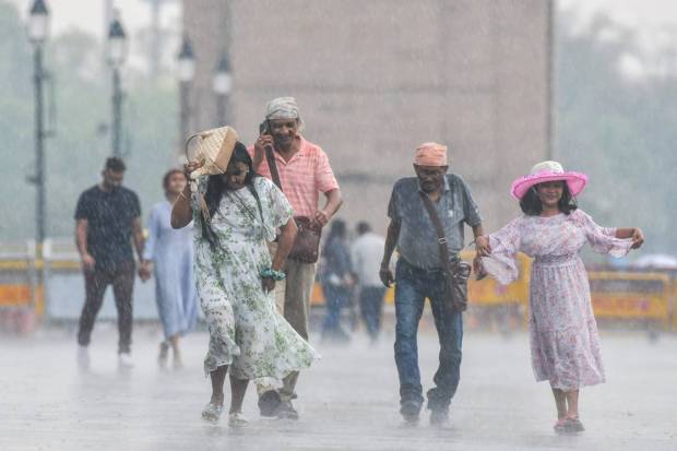 New Delhi: People protecting themselves from rain walk on a road at India Gate, in New Delhi. (PTI Photo)