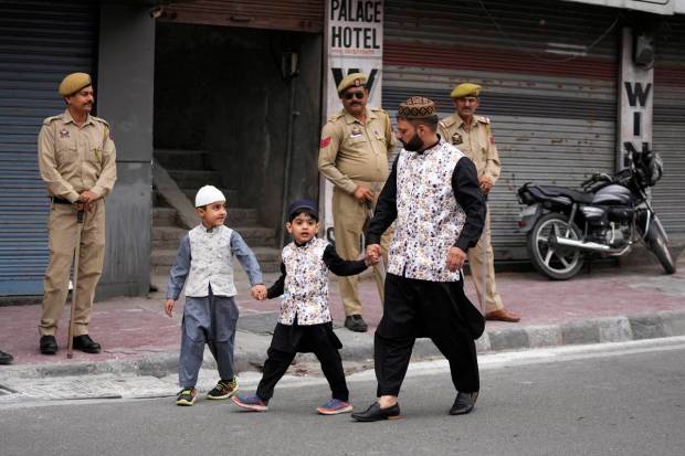 Policemen stand guard as a Muslim family returns home after offering Eid al-Fitr prayers in Jammu, India. (AP Photo)