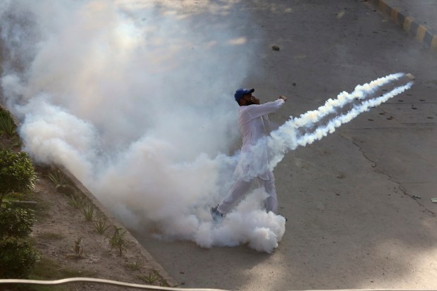 A supporter of Pakistan's former Prime Minister Imran Khan hurls back a tear gas shell toward police as he with others protesting against the arrest of their leader. (AP Photo)