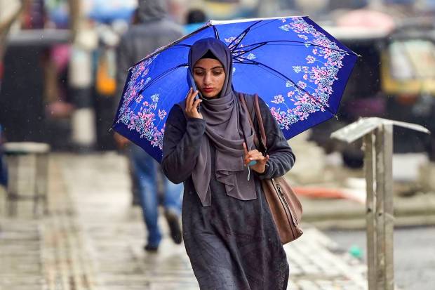 Srinagar: A young woman walks down a road amid rainfall, in Srinagar. (PTI Photo)