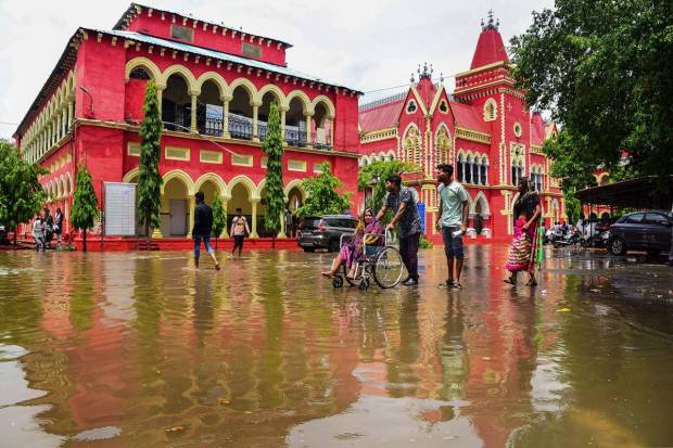 Jabalpur: A wheelchair-bound patient being assisted by her relative to cross the waterlogged campus of Government Victoria Hospital following rainfall, in Jabalpur. (PTI Photo)