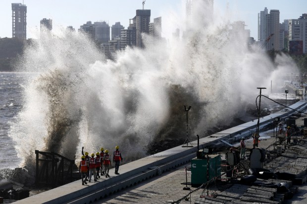 Coastal road workers walk as waves hit the city's waterfront during high tide in the Arabian Sea at Marine Drive in Mumbai. The Bombay Municipal Council is making arrangements to tackle the approach of Cyclone Biparjoy. (AP Photo)