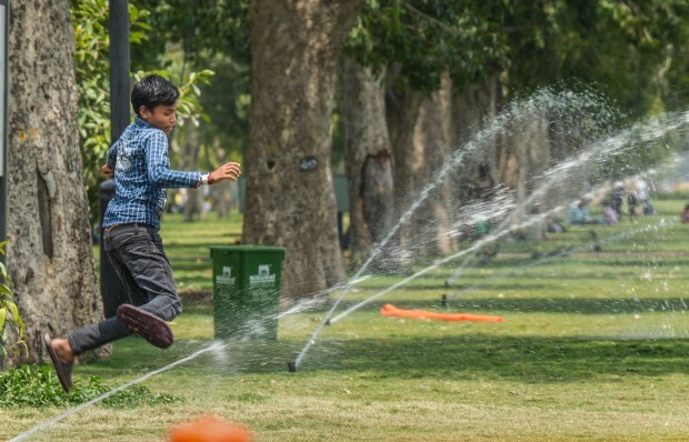 A boy plays near water fountains at an India Gate lawn during a hot summer afternoon in New Delhi. (PTI Photo)