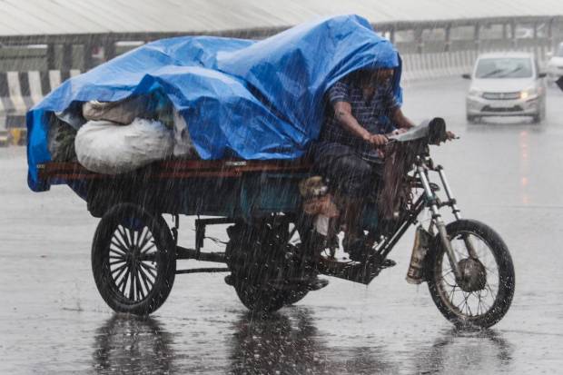 Gurugram: A man rides a tricycle on a road amid rain, in Gurugram. (PTI Photo)