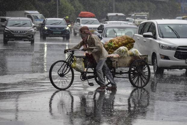 A vegetable vendor walks through traffic amid heavy rainfall in Gurugram. (Image: PTI)